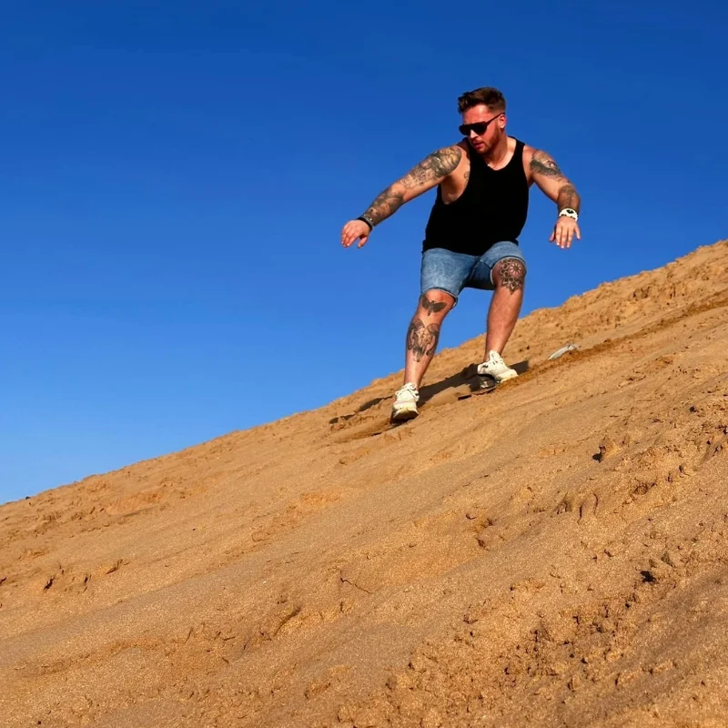Man enjoying sandboarding in Agadir on golden dunes under blue sky – sandboarding Agadir experience