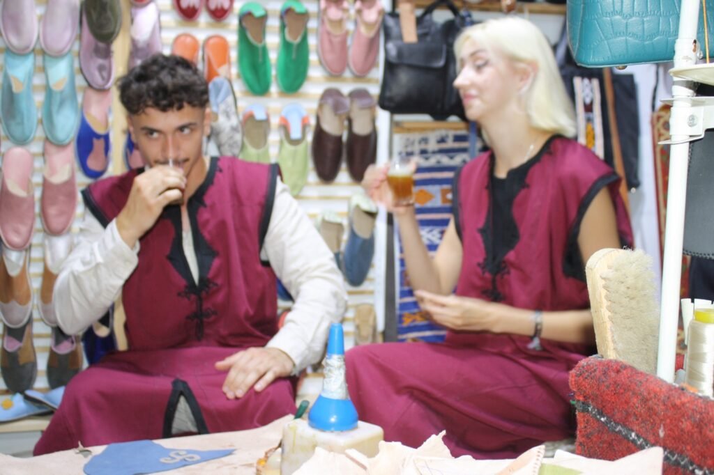 Two travellers in workshop attire drinking tea at a leather babouche workshop in Agadir