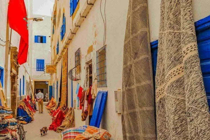 Narrow medina alley in Essaouira with handwoven rugs hanging on blue-shuttered walls
