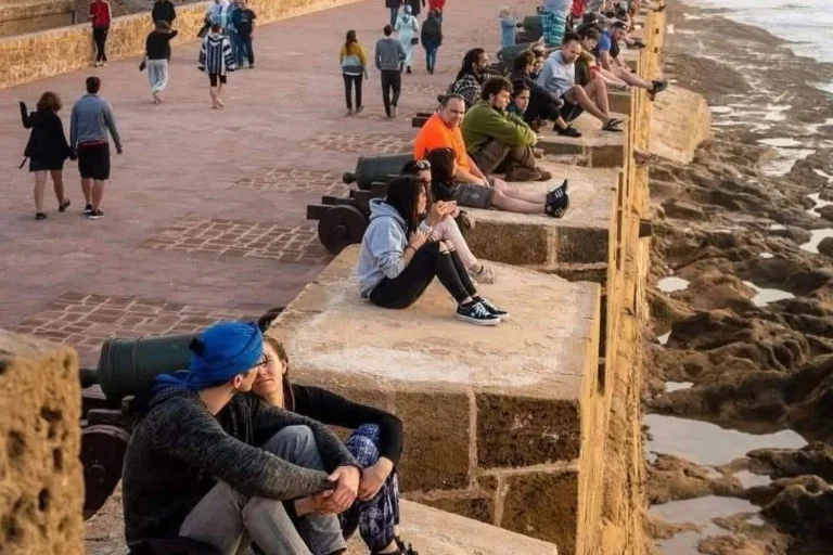 Travelers sitting on the Essaouira ramparts watching the sunset over the Atlantic