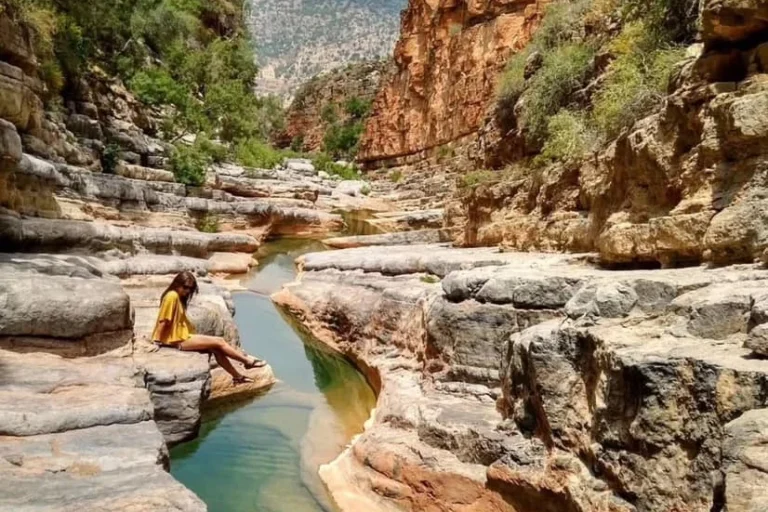 Visitor sitting on a rock ledge above a turquoise pool in Paradise Valley