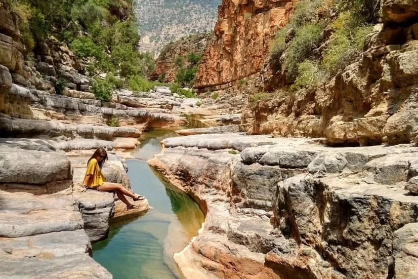 Visitor sitting on a rock ledge above a turquoise pool in Paradise Valley