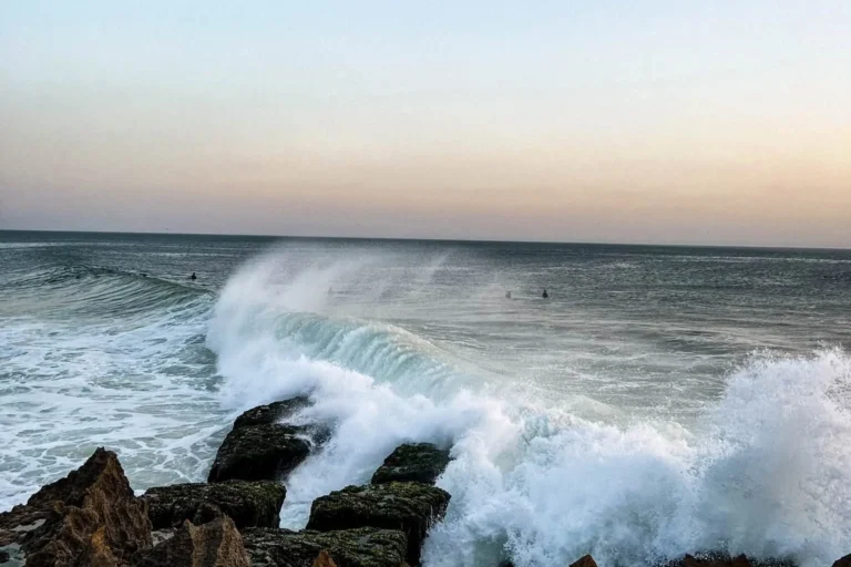 Surfers sitting in the lineup at Agadir as a wave breaks at sunset