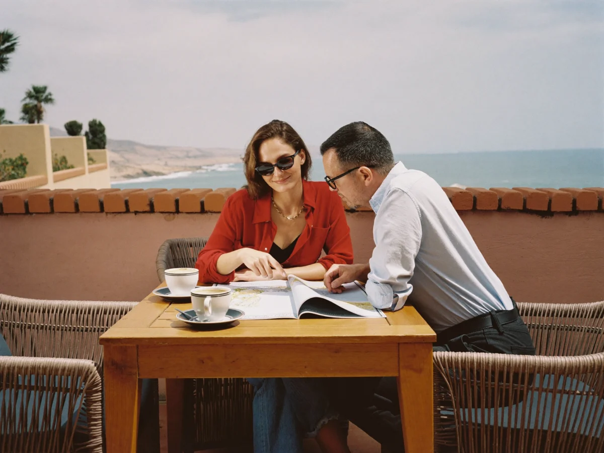 Two travelers reviewing a paper map together at an outdoor coastal cafe table