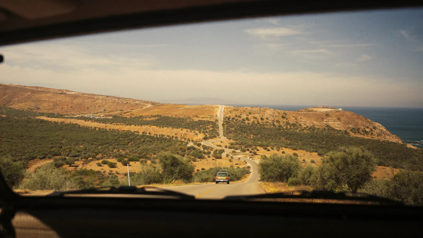 Car driving along a winding coastal road through dry hills in southern Morocco